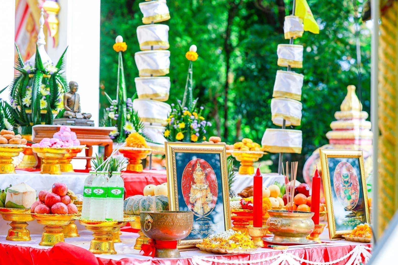 Thai offering altar with framed amulet images, candles, fruit, incense featuring Thao Wessuwanno Bandarn Patthanapon
