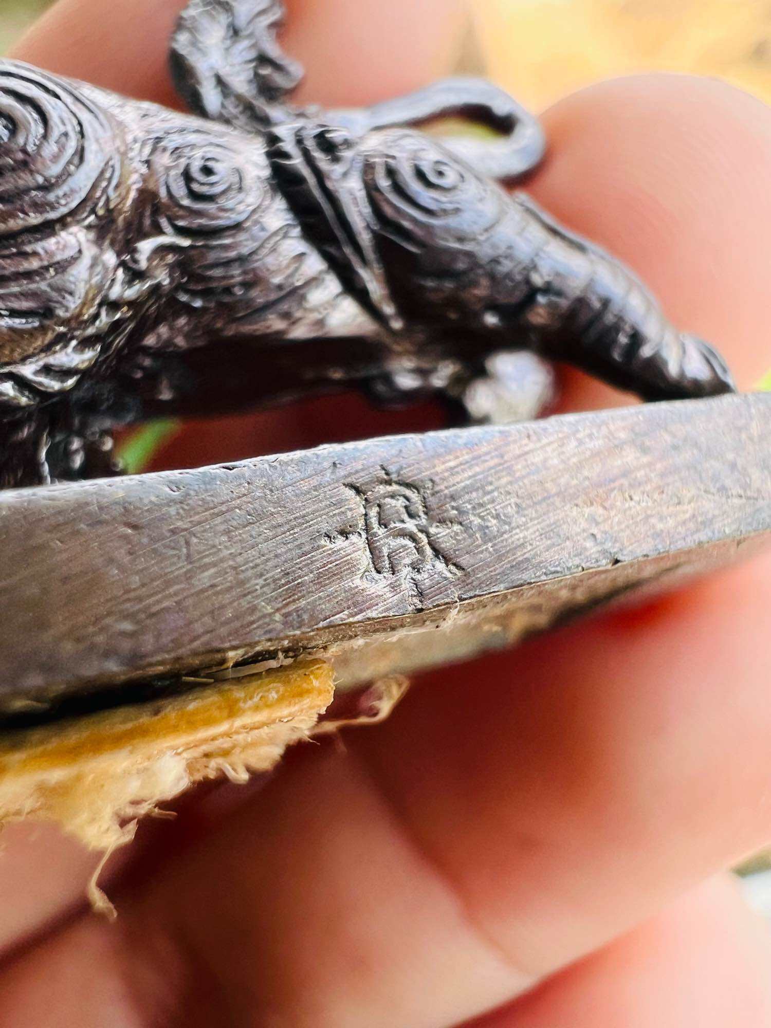 Close up of small detailed metal elephant on a stamped base showing wear Wua Thanu Thai protection amulet