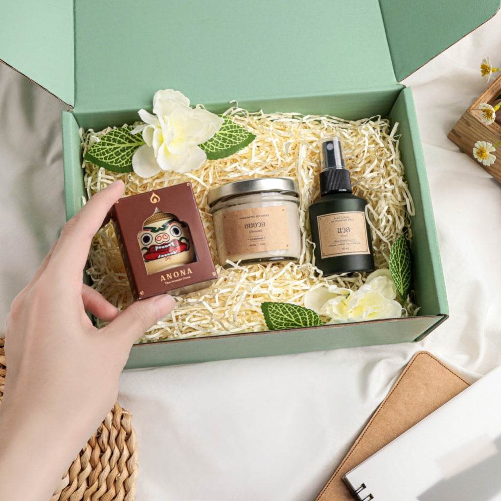 Hand holding herbal balm soy candle gift box with natural skincare products and flowers in green packaging