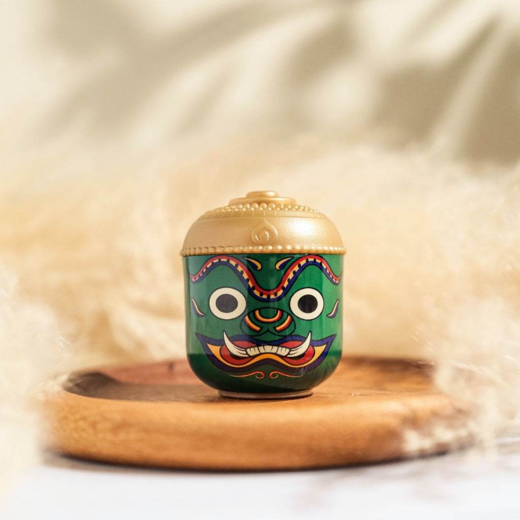 Thai herbal aroma sachet with traditional green mask design and gold lid on wooden tray