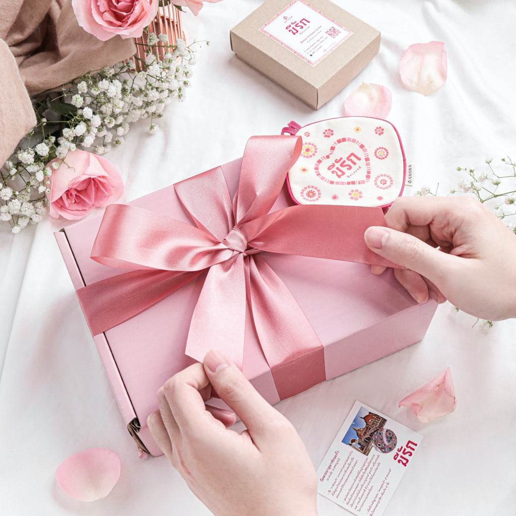 Valentine's day gift box for her with pink ribbon and floral decorations on white surface