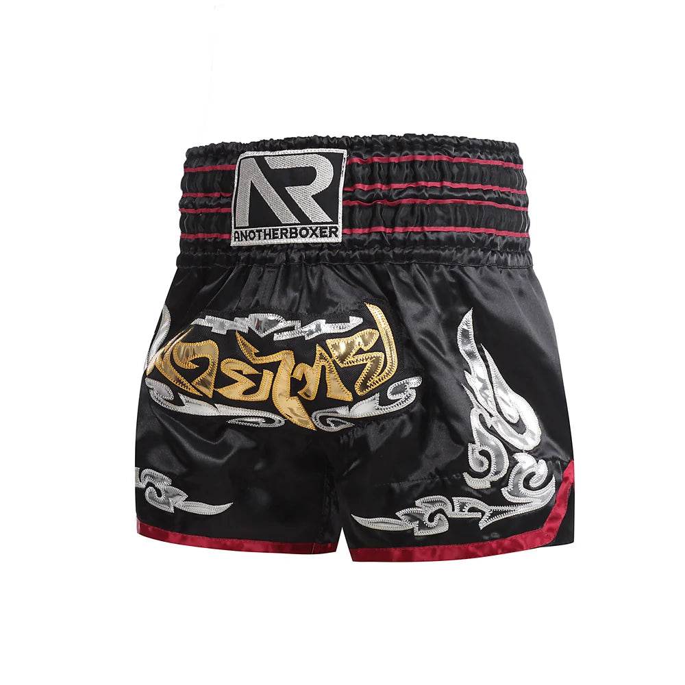 Black Muay Thai boxing shorts with gold Thai script silver ornamental patterns and red trim elastic waistband