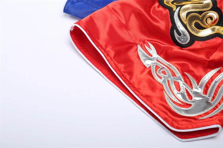 Red satin Muay Thai boxing shorts with silver and gold embroidery white piping close up by Thai Blessing Co