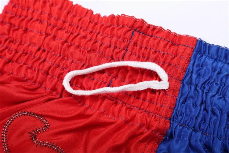 Red and blue Muay Thai boxing shorts close up showing elastic waistband white drawstring and embroidery