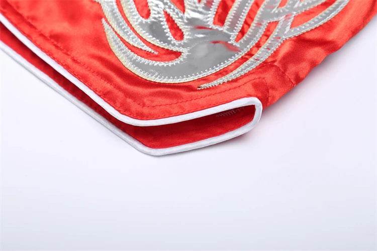 Red satin Muay Thai boxing shorts close up with silver embroidered design and white piping hem