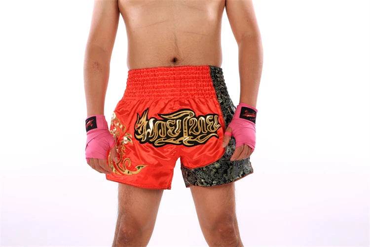 Male model wearing red and black Muay Thai boxing shorts with gold script and pink hand wraps