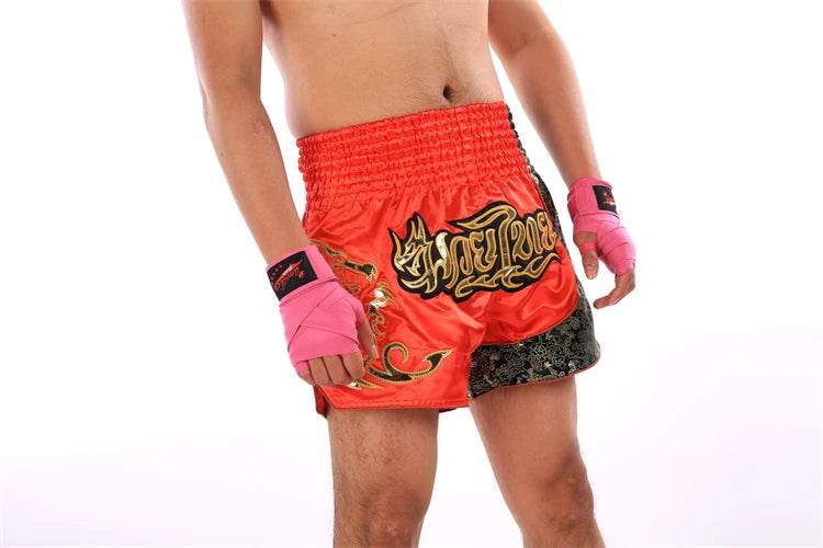 Thai Blessing Co red Muay Thai boxing shorts with gold Thai script and black side trim worn by male fighter