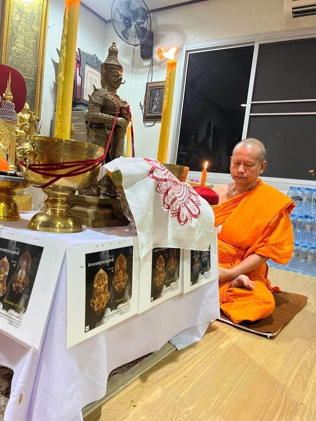 Buddhist monk in orange robe meditating near altar with authentic Thai blessed amulet and candles
