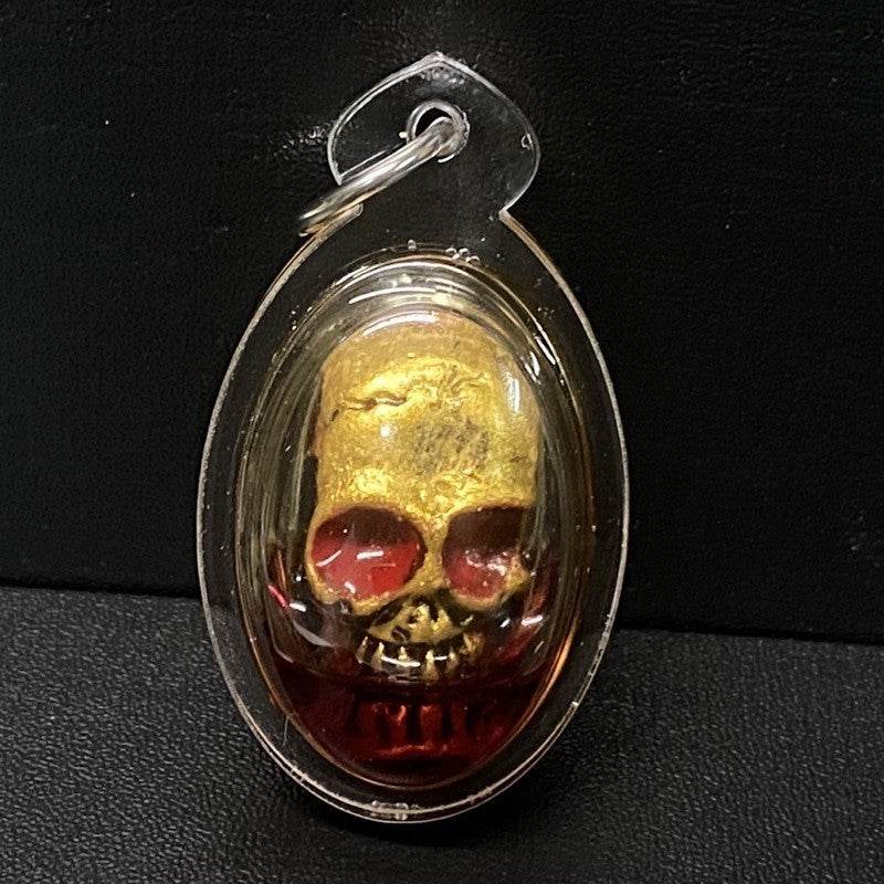 Authentic Thai spirit amulet featuring a golden skull encased in protective plastic for spiritual blessings