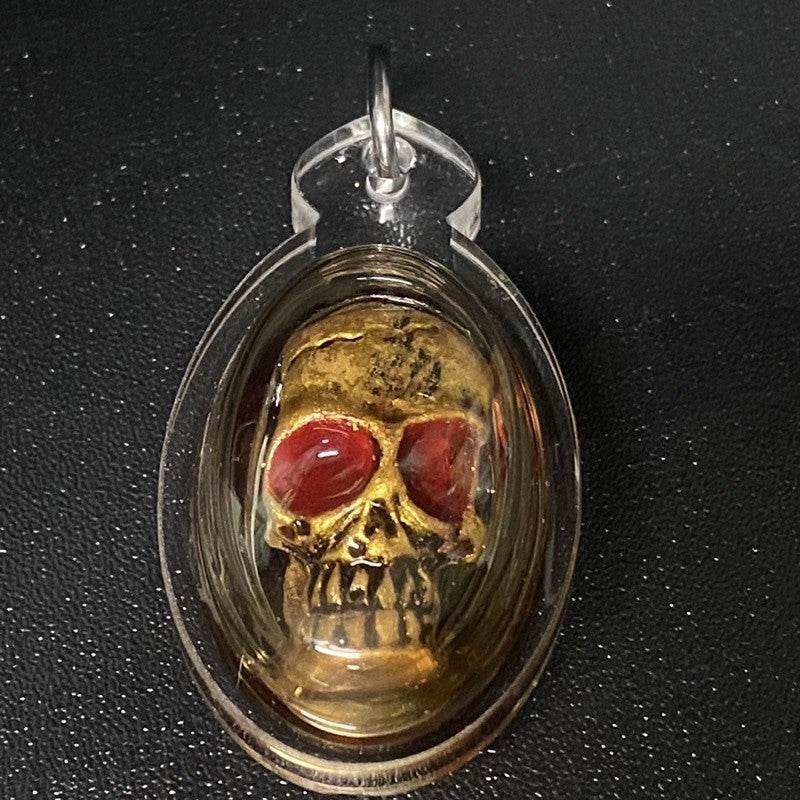 Authentic Thai spirit amulet featuring a golden skull design with red accents for spiritual protection