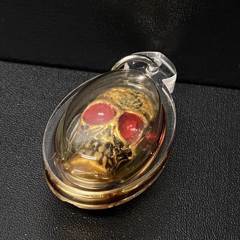 Authentic Thai spirit amulet encased in a clear protective shell featuring a skull design