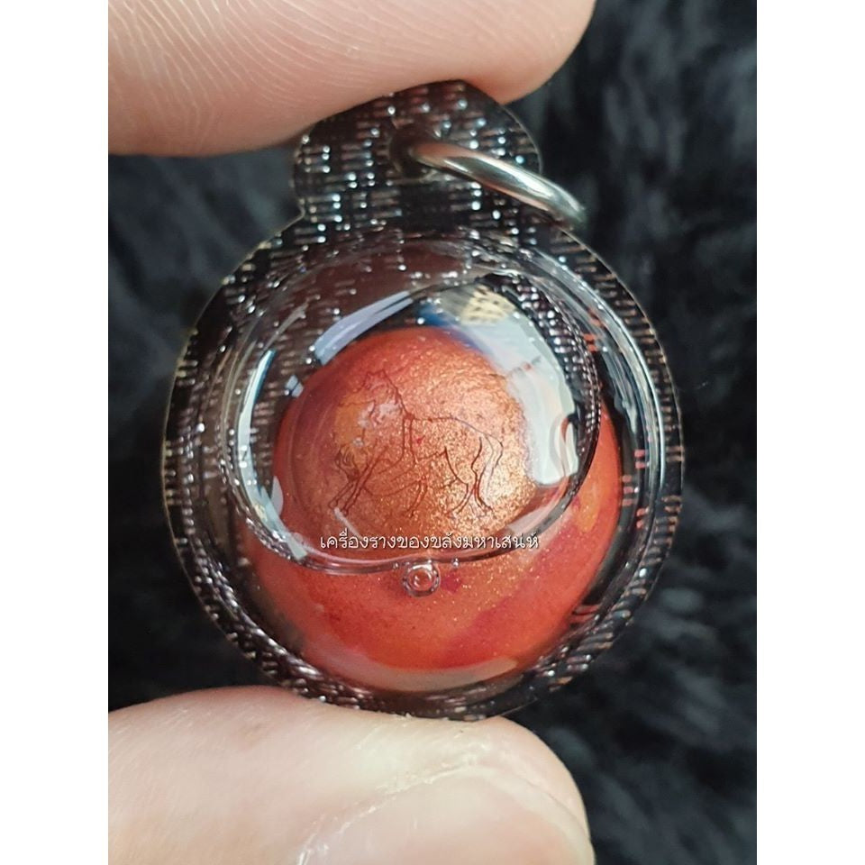 Authentic Thai spiritual charm ball pendant with black woven casing held between fingers
