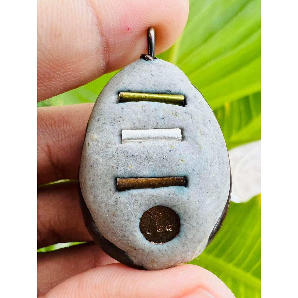 Close-up of Bai Kae Supreme Protection amulet with metallic inserts held between fingers