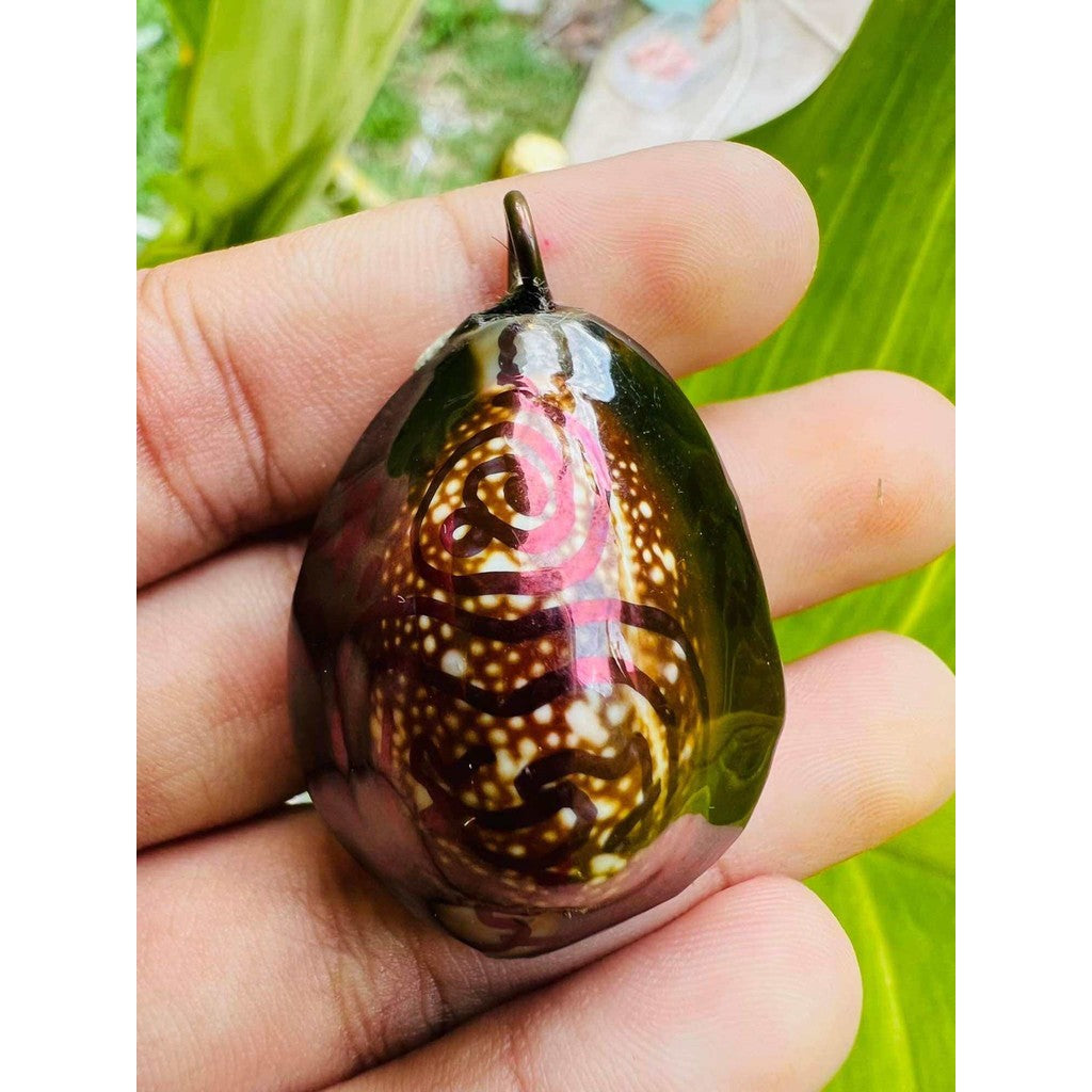 Hand holding a Bai Kae Supreme Protection amulet with intricate design and dark glossy finish