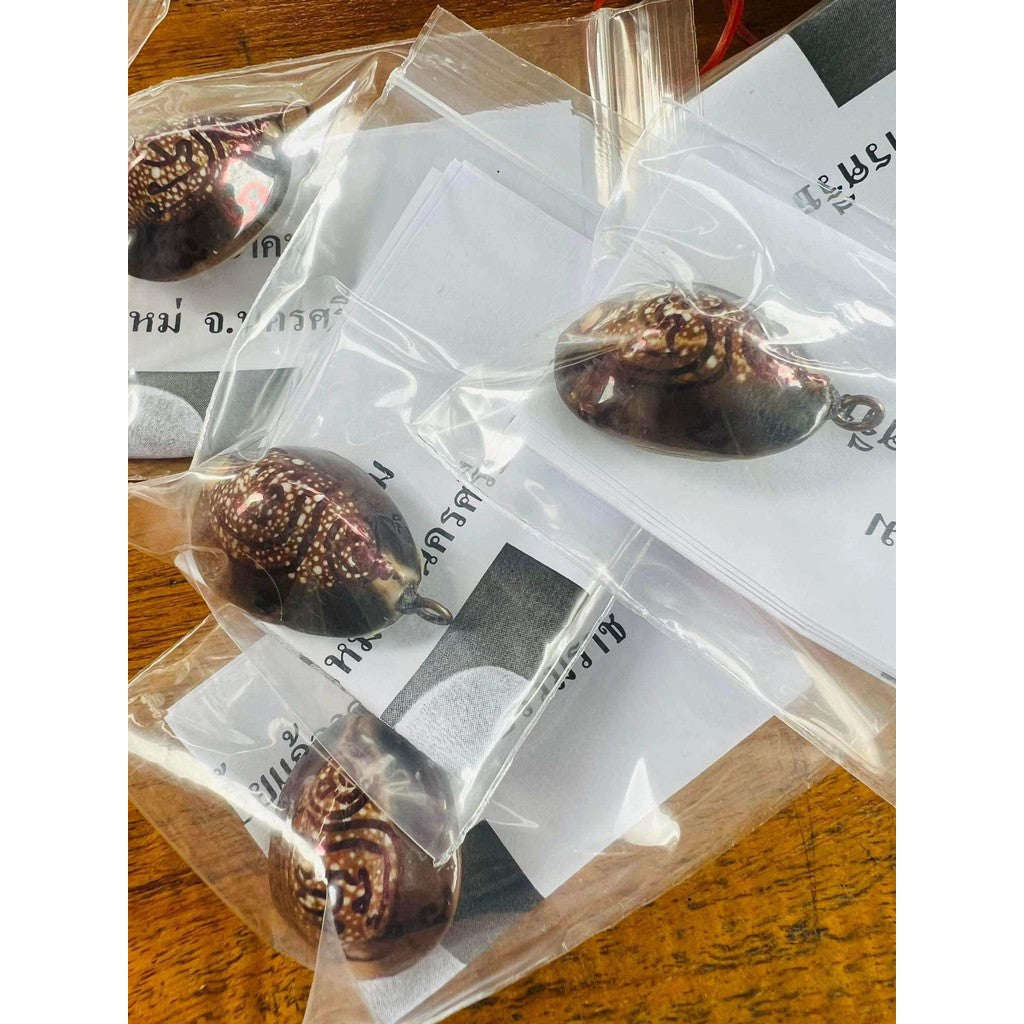 Bai Kae Supreme Protection amulet with intricate designs packaged in clear plastic bags on wooden surface