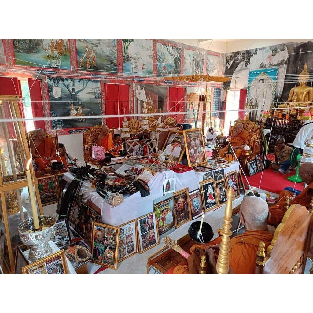 Bai Kae Supreme Protection amulet displayed in a Thai temple surrounded by monks and religious artifacts