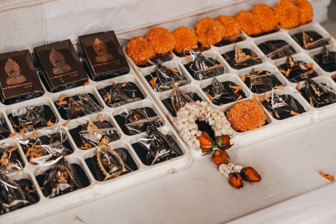 Phra Nak Prok statue bronze amulets in black gift boxes displayed on tray with marigold and jasmine garlands