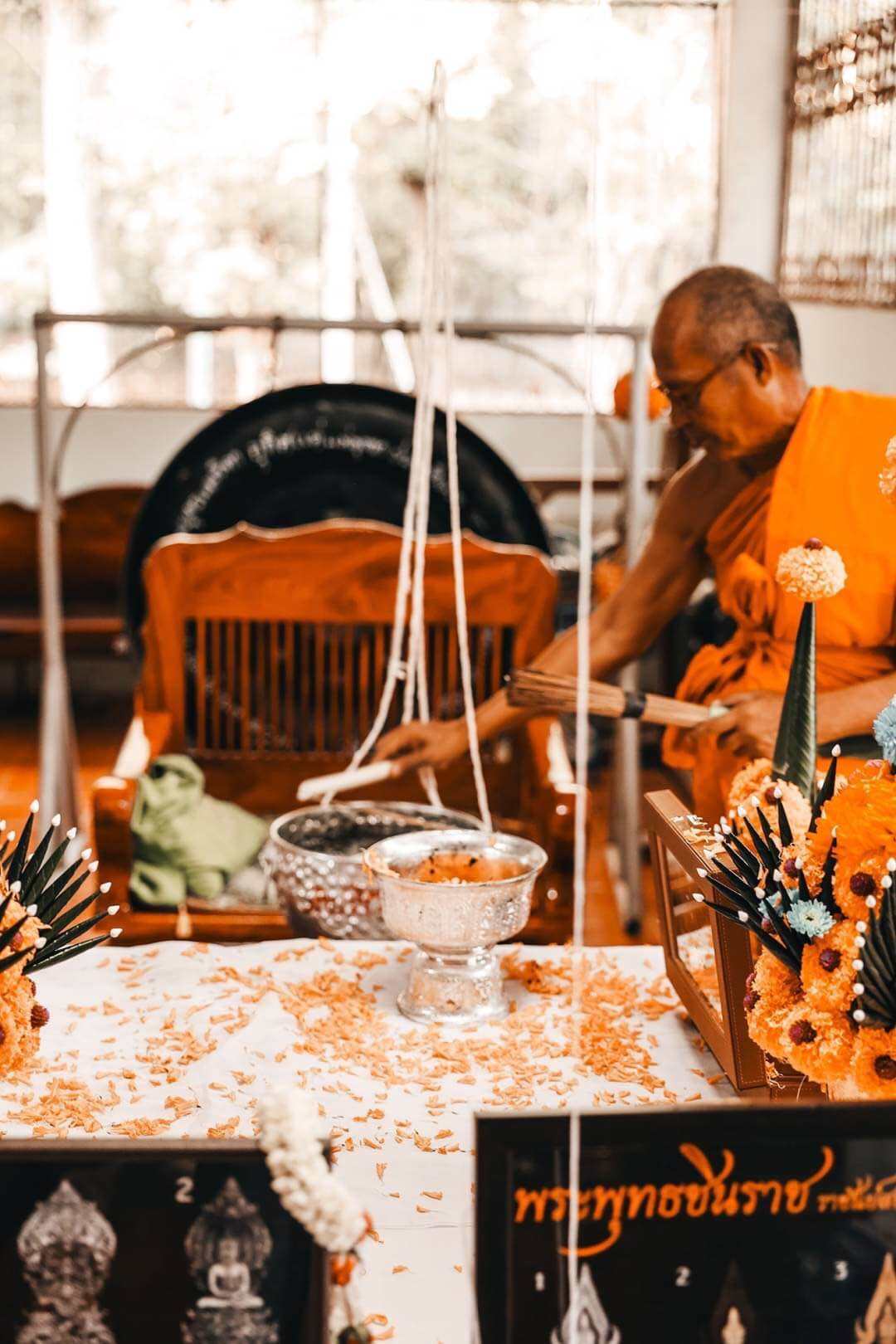 Thai monk blessing Phra Nak Prok statue bronze amulet on altar with marigold offerings and ceremony