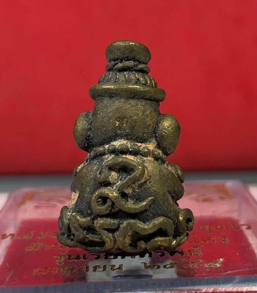 Bronze Ruesi amulet on display box with Thai script and red backdrop Borom Kru Phu Phu Ruesi Amulet Wealth Calling Edition