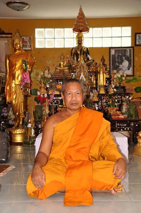 Monk in orange robes surrounded by statues, representing the authentic palad khik amulet tradition