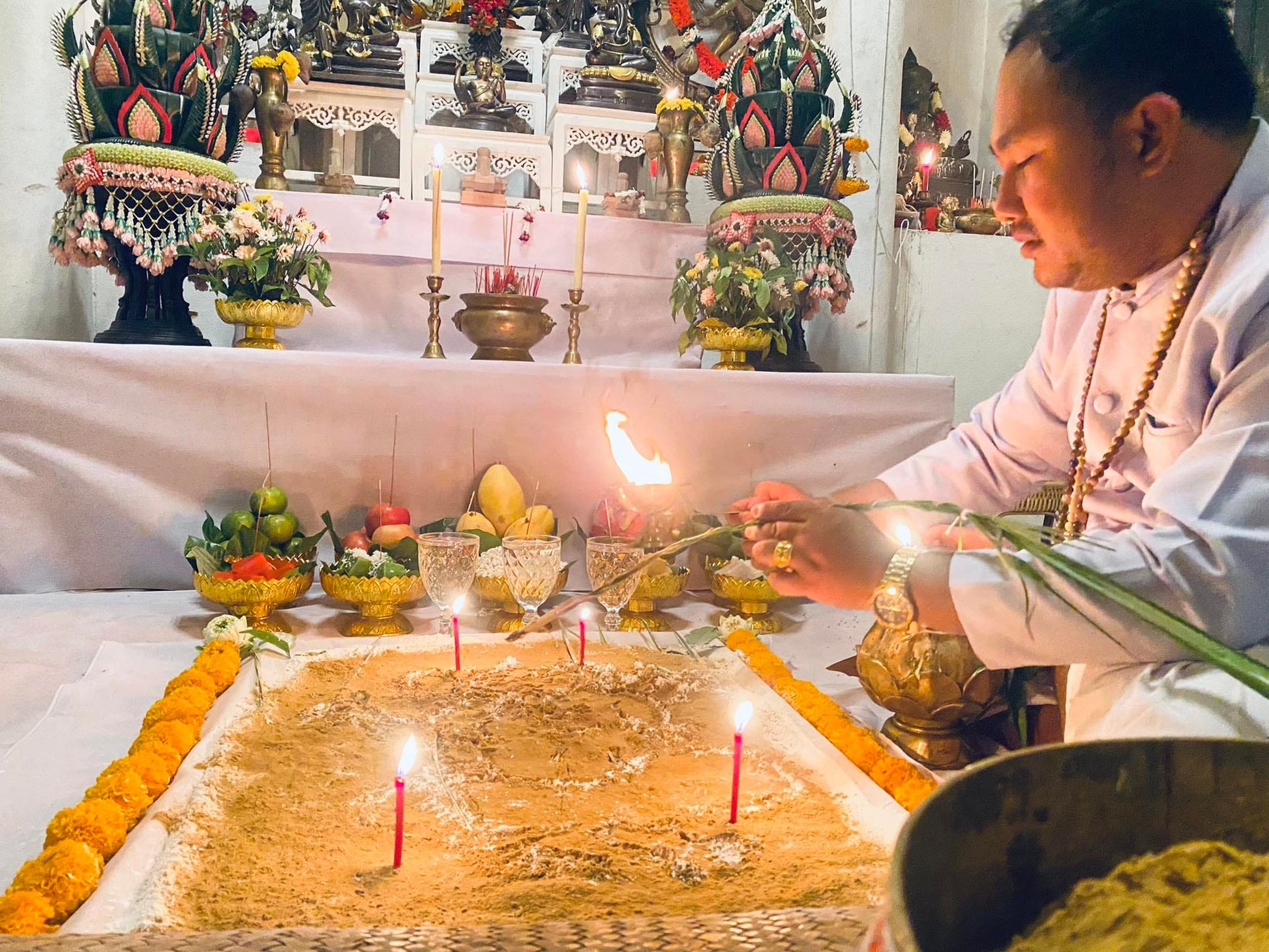 Ceremonial scene featuring a monk performing a ritual to cleanse negative energy Thai amulet with candles and offerings
