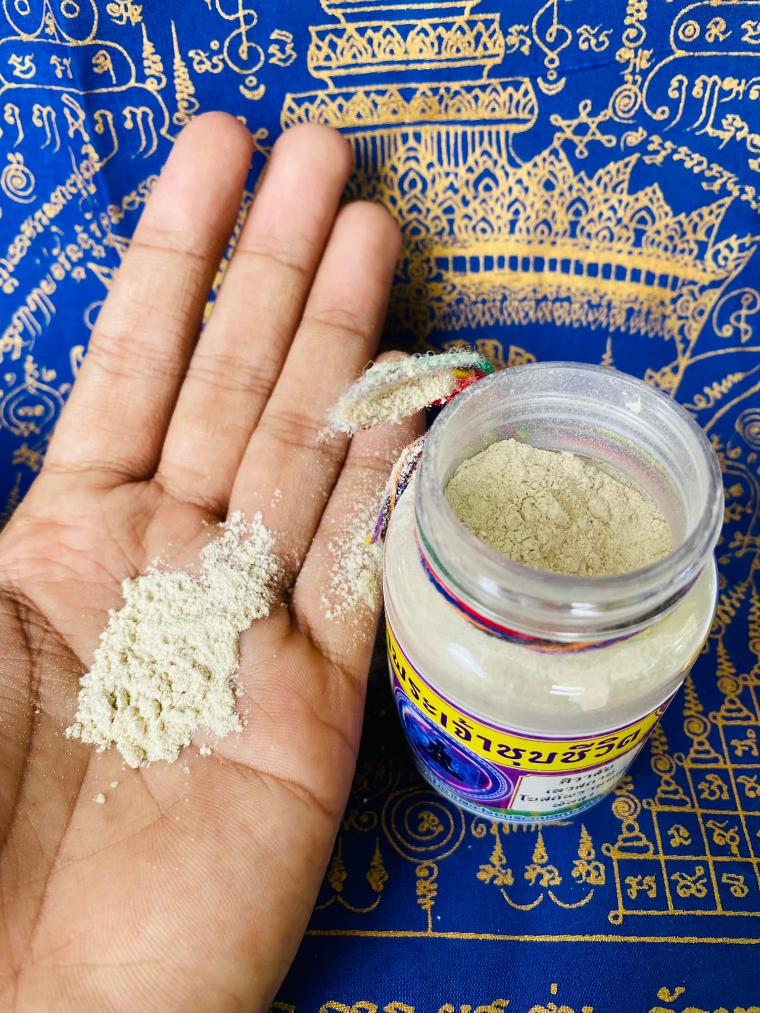 Hand holding powder from Thai Blessing Co cleanse negative energy Thai amulet in a jar