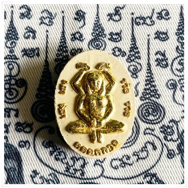 Divine attraction Thai charm featuring a golden frog amulet on a patterned fabric background