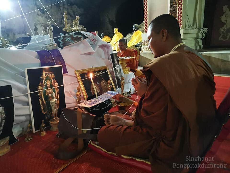 Monk holding Ei Khai Phaya Kai bronze amulet during a traditional Buddhist ceremony indoors