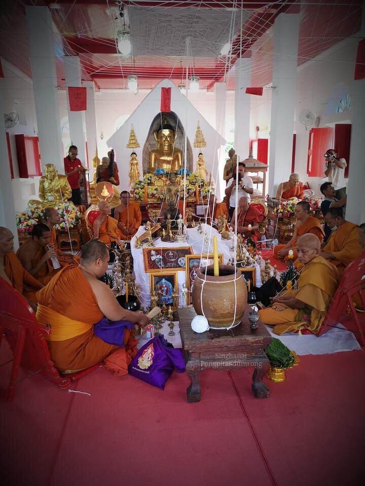 Monks performing a traditional ceremony in a temple with Ei Khai Phaya Kai bronze amulet on display