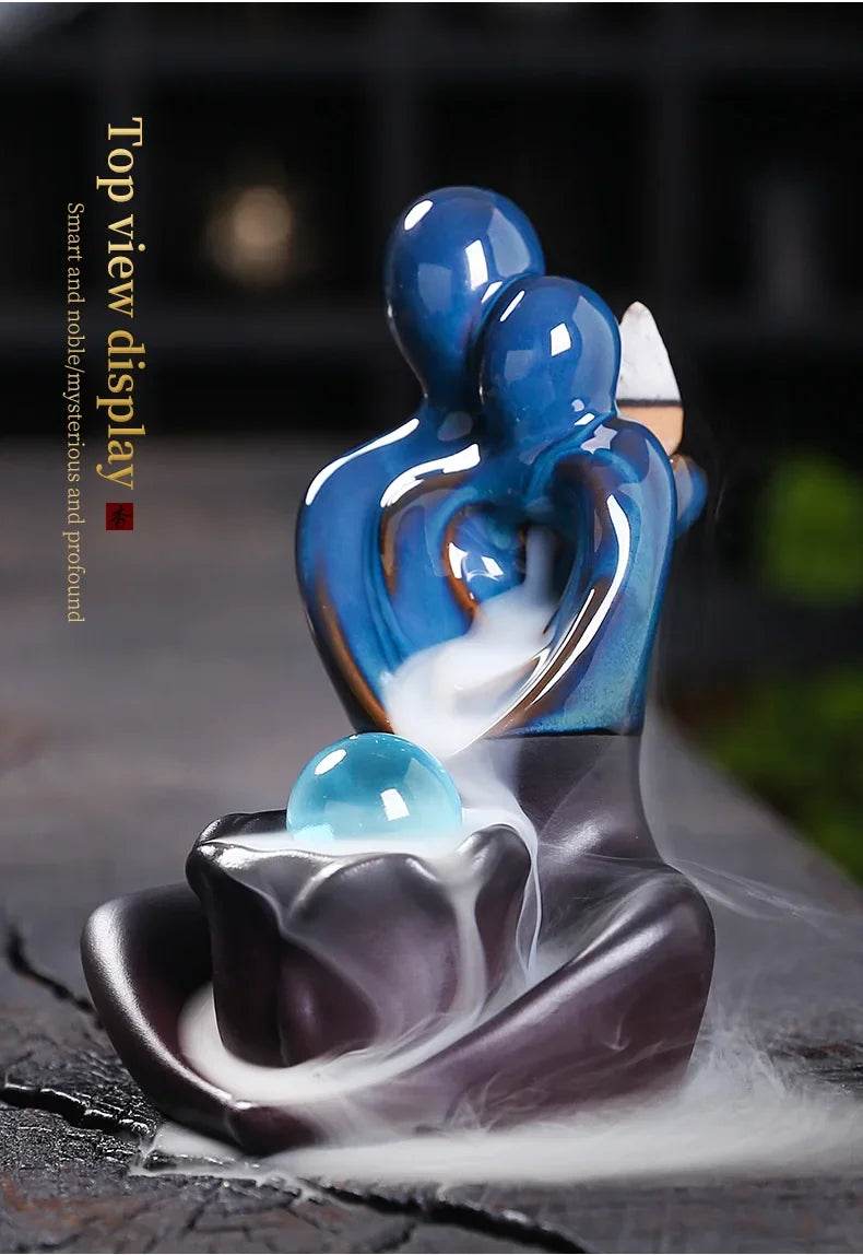 Blue ceramic backflow incense burner with glossy abstract embracing figures and cascading smoke over glass orb