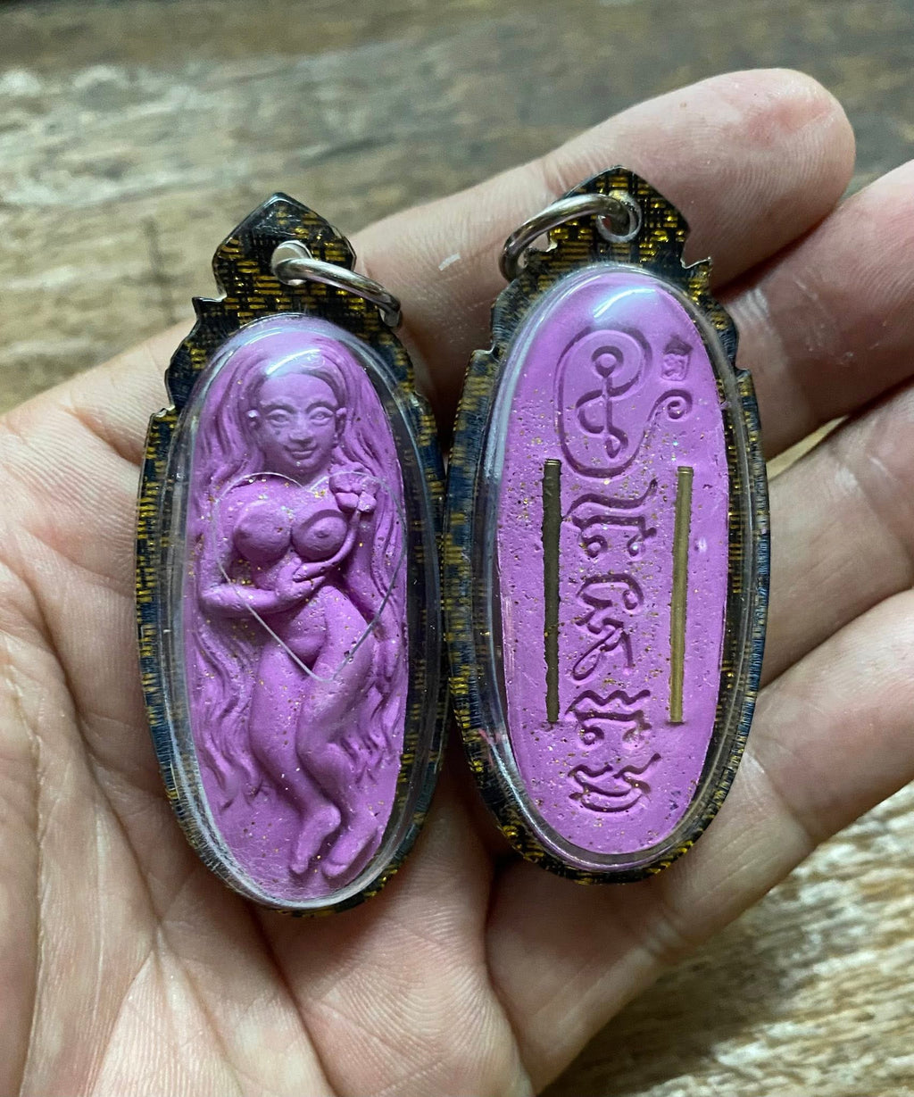 Enchanting Grace Mae Nuea Hom charm purple amulet with detailed figure and script held in hand by Thai Blessing Co