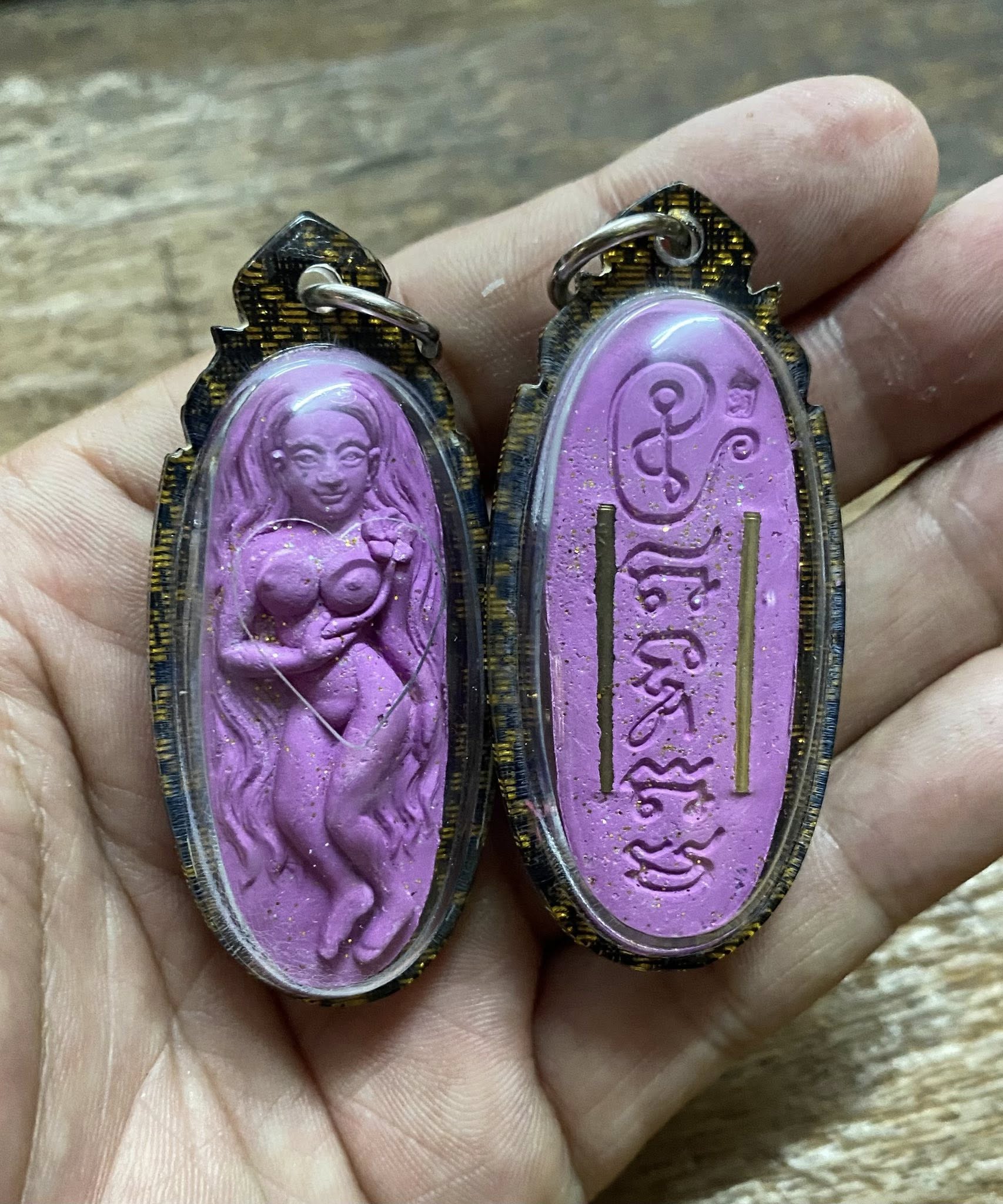 Enchanting Grace Mae Nuea Hom charm purple amulet with detailed figure and script held in hand by Thai Blessing Co