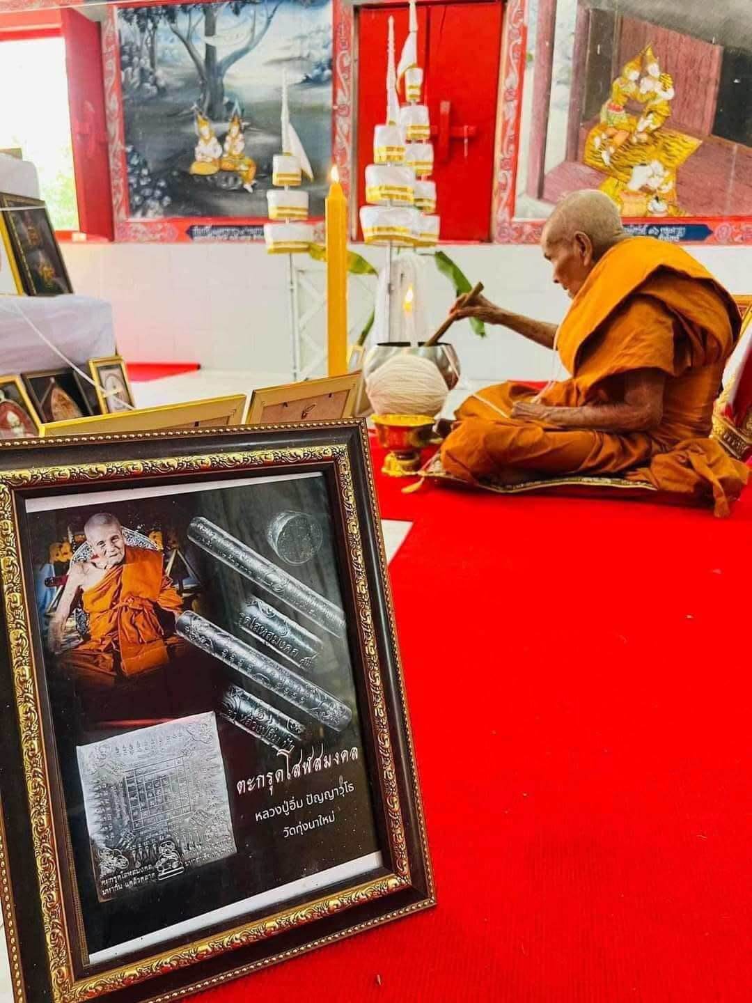 First edition collectible Thai blessing charm displayed in a frame near a monk performing a religious ceremony