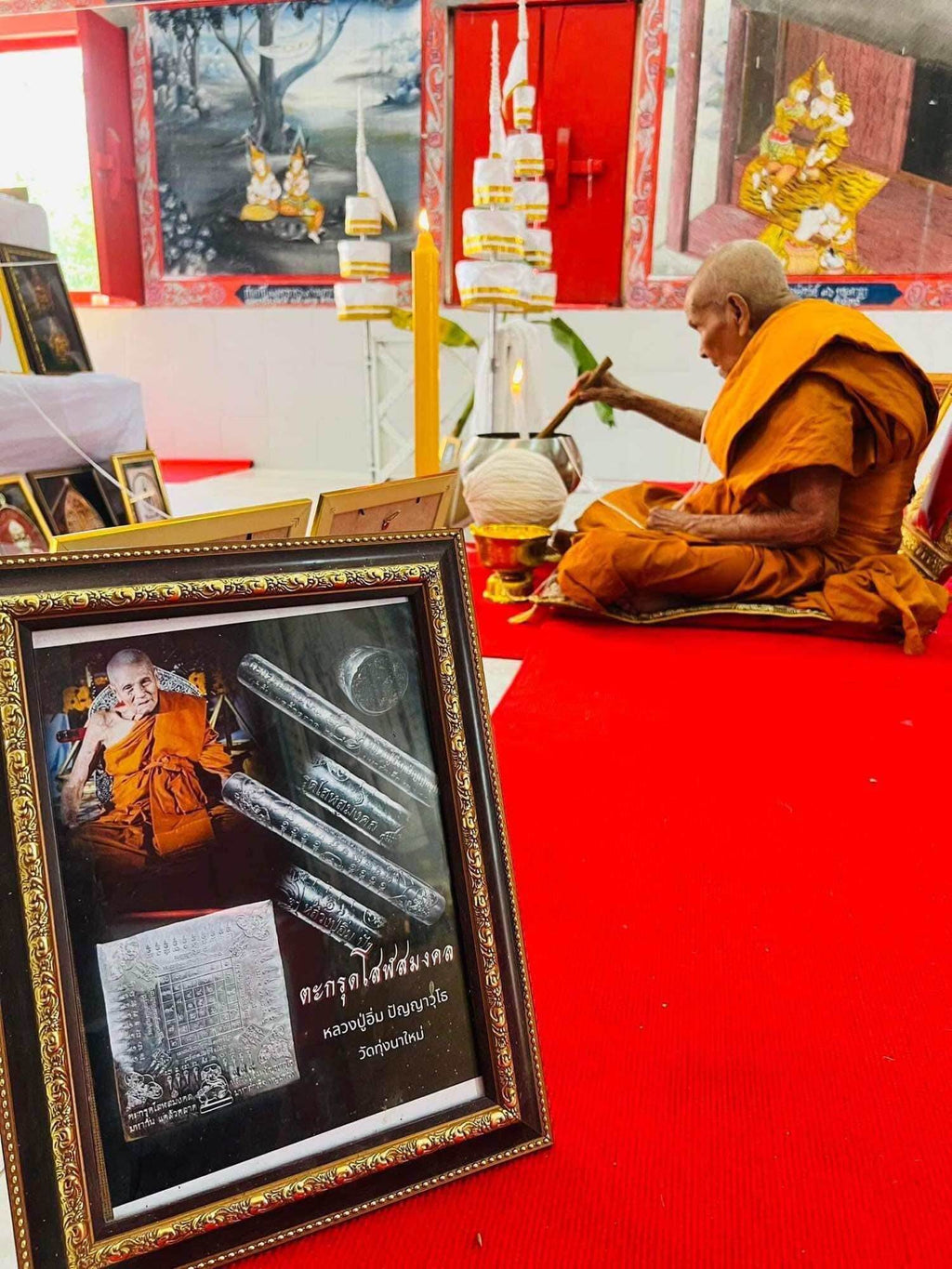 First edition collectible Thai blessing charm displayed in a framed photo with a monk performing a traditional blessing ritual