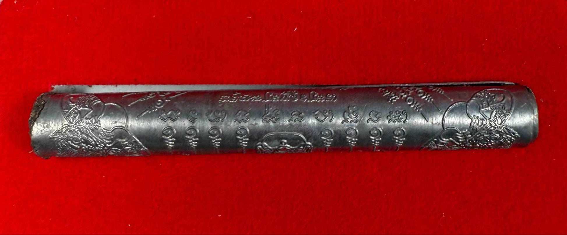 First edition collectible Thai blessing charm in metal form with intricate engravings on red background