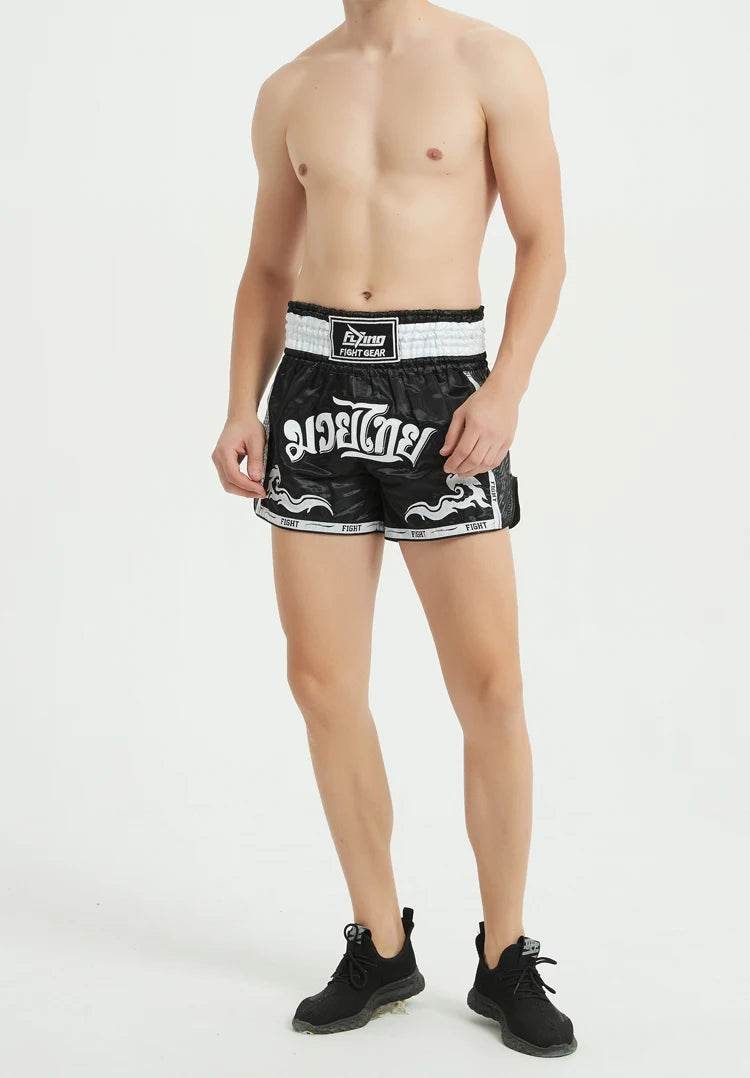 Male model wearing black and white Muay Thai boxing shorts with elastic waistband and Thai script design