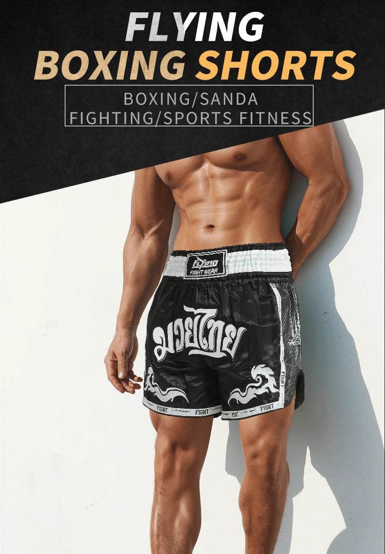 Muscular male model wearing black satin Muay Thai boxing shorts with white Thai script and elastic waist