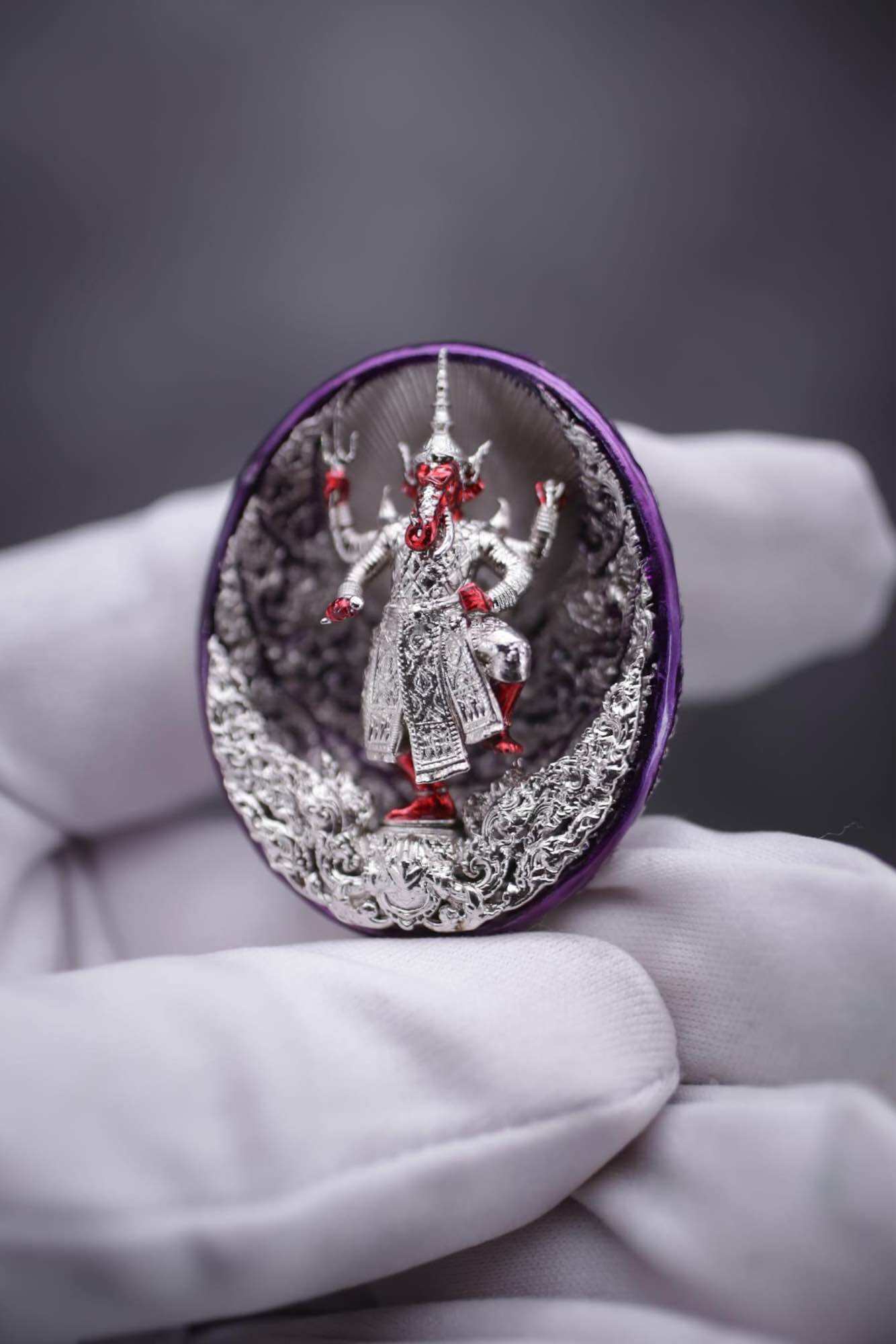 Ganesh coin amulet for wealth featuring a detailed silver and red statue in a decorative setting