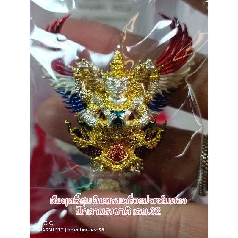 Gold and colorful Garuda amulet from Thailand held in hand with intricate detailing