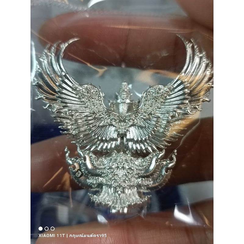 Silver Garuda amulet from Thailand with intricate detailed wings held between fingers by Thai Blessing Co