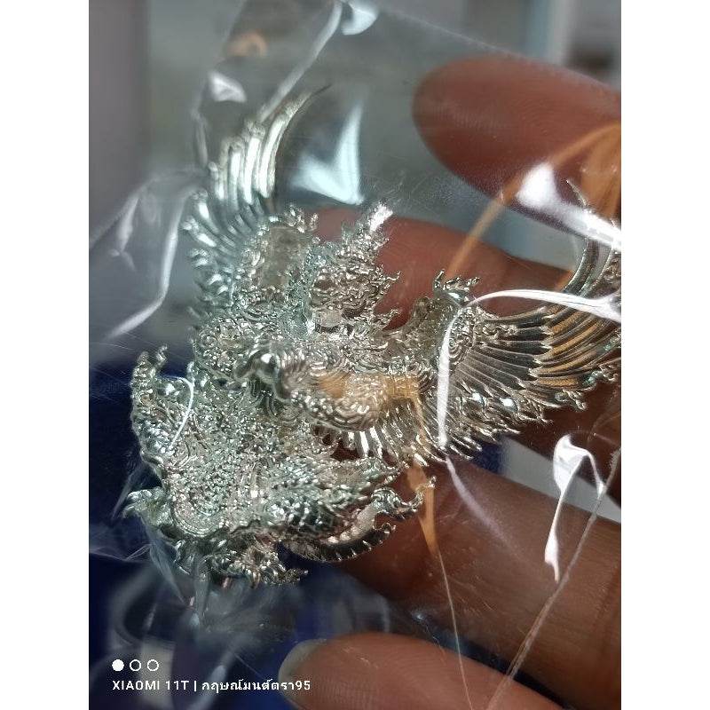 Silver Garuda amulet from Thailand held in hand wrapped in clear plastic packaging