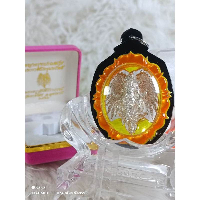 Garuda Parameswara amulet with intricate silver design in orange and black casing displayed on clear stand