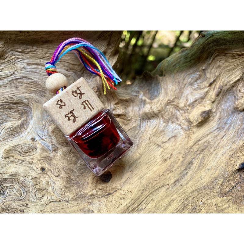 Thai charm oil for prosperity in small glass bottle with red oil wooden cap engraved with Thai script and rainbow tassel