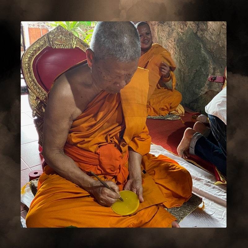 Thai monk blessing a small amulet with Thai charm oil for prosperity in temple ceremony