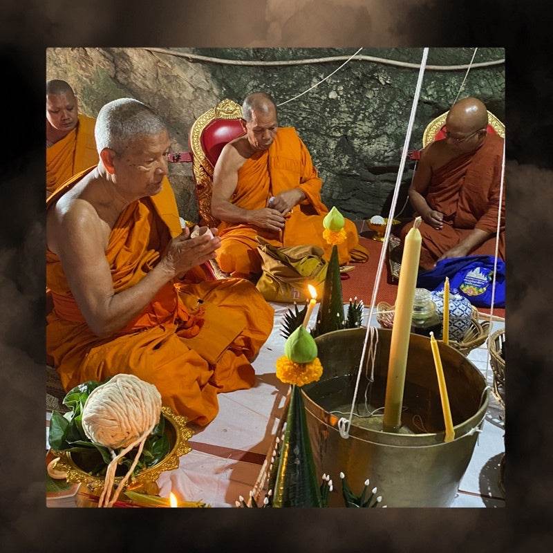 Monks blessing Thai charm oil for prosperity in a traditional Thai ritual with candles and offerings