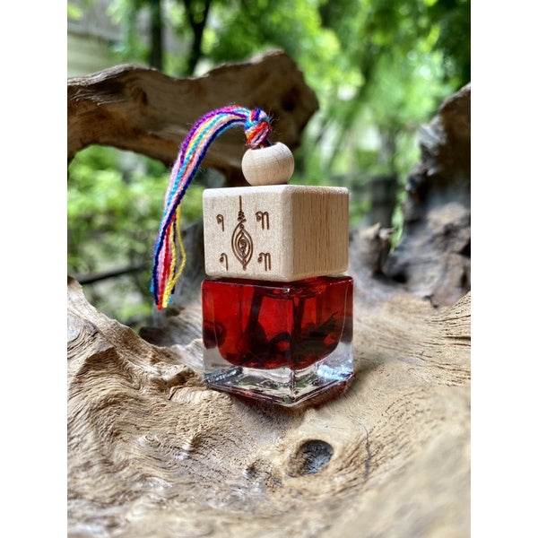 Thai charm oil for prosperity red glass bottle with wooden engraved cap and multicolor cord tassel by Thai Blessing Co