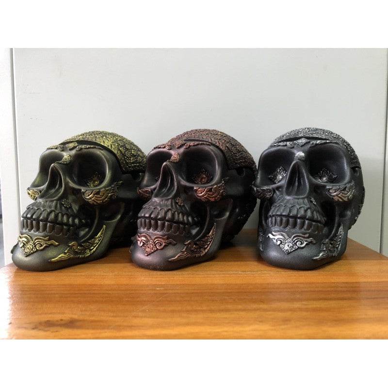 Handcrafted gold skull ashtray displayed alongside bronze and silver skull ashtrays on wooden surface
