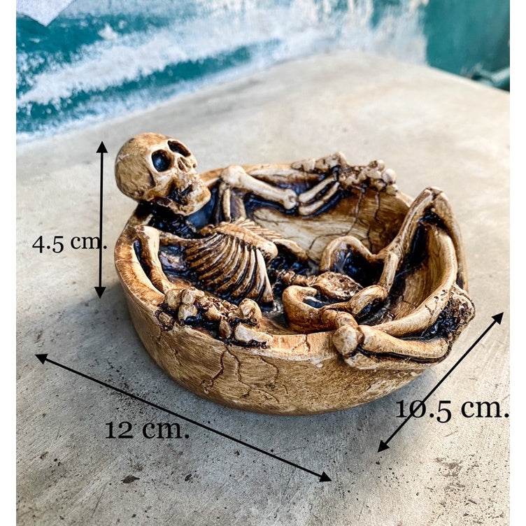 Handcrafted resin skeleton ashtray with detailed skeleton figure lying in a round bowl measuring 12 by 10.5 by 4.5 cm