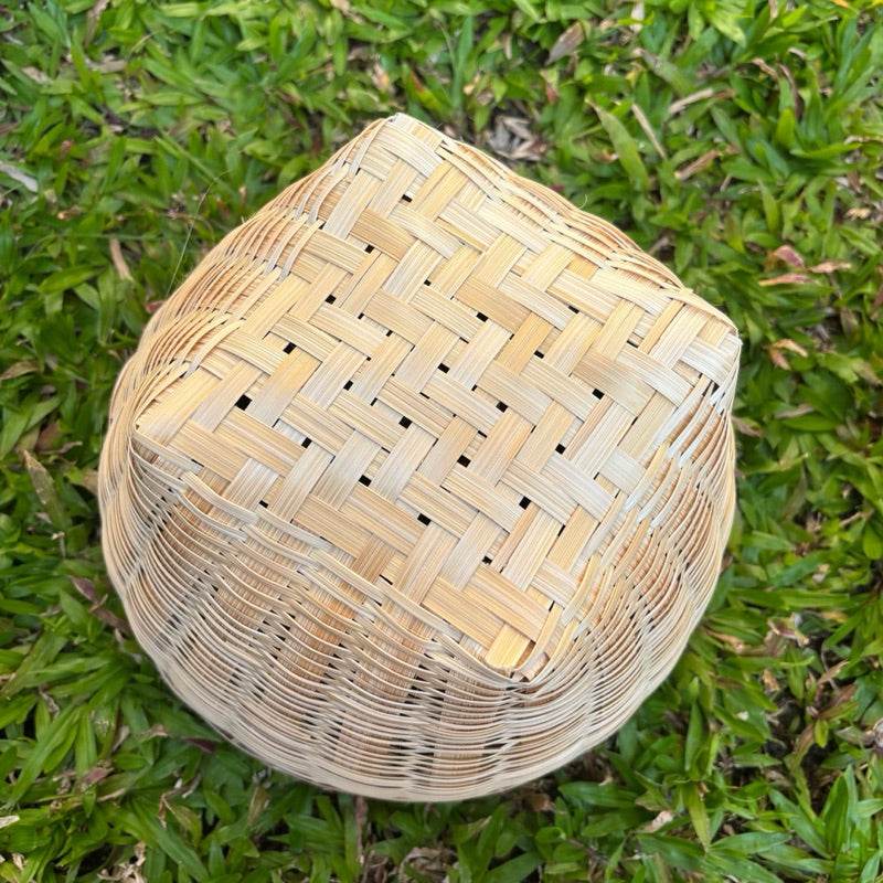 Handmade Thai bamboo basket with woven pattern displayed on green grass from One-Sake.com
