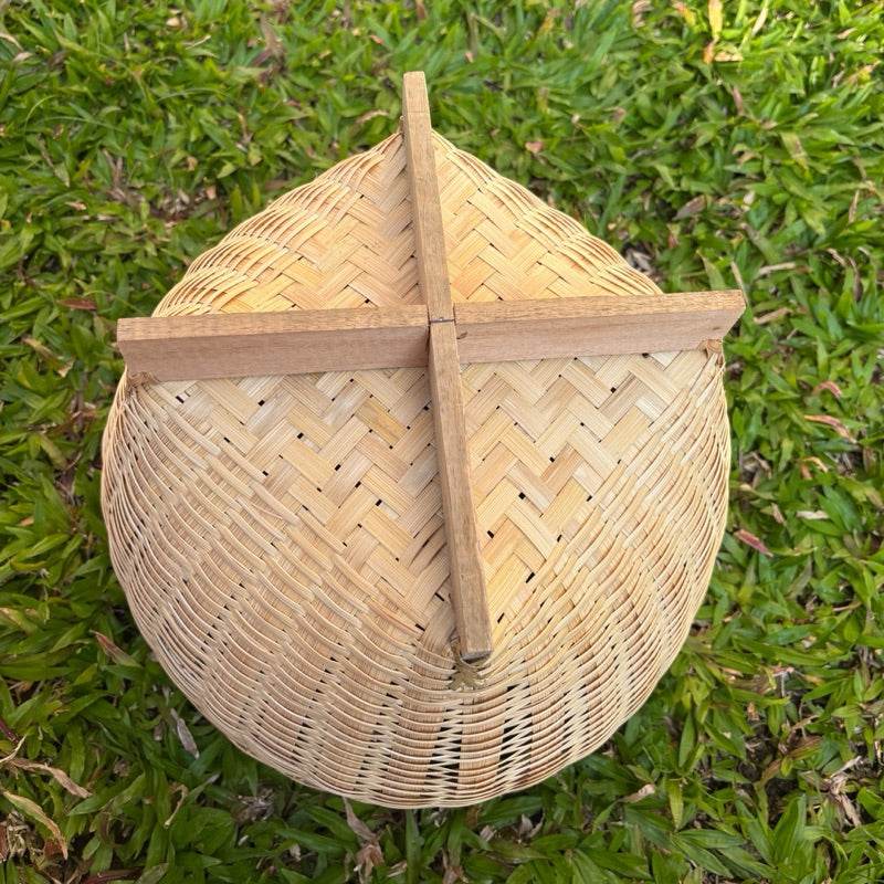 Handmade Thai bamboo basket with wooden cross support on green grass background